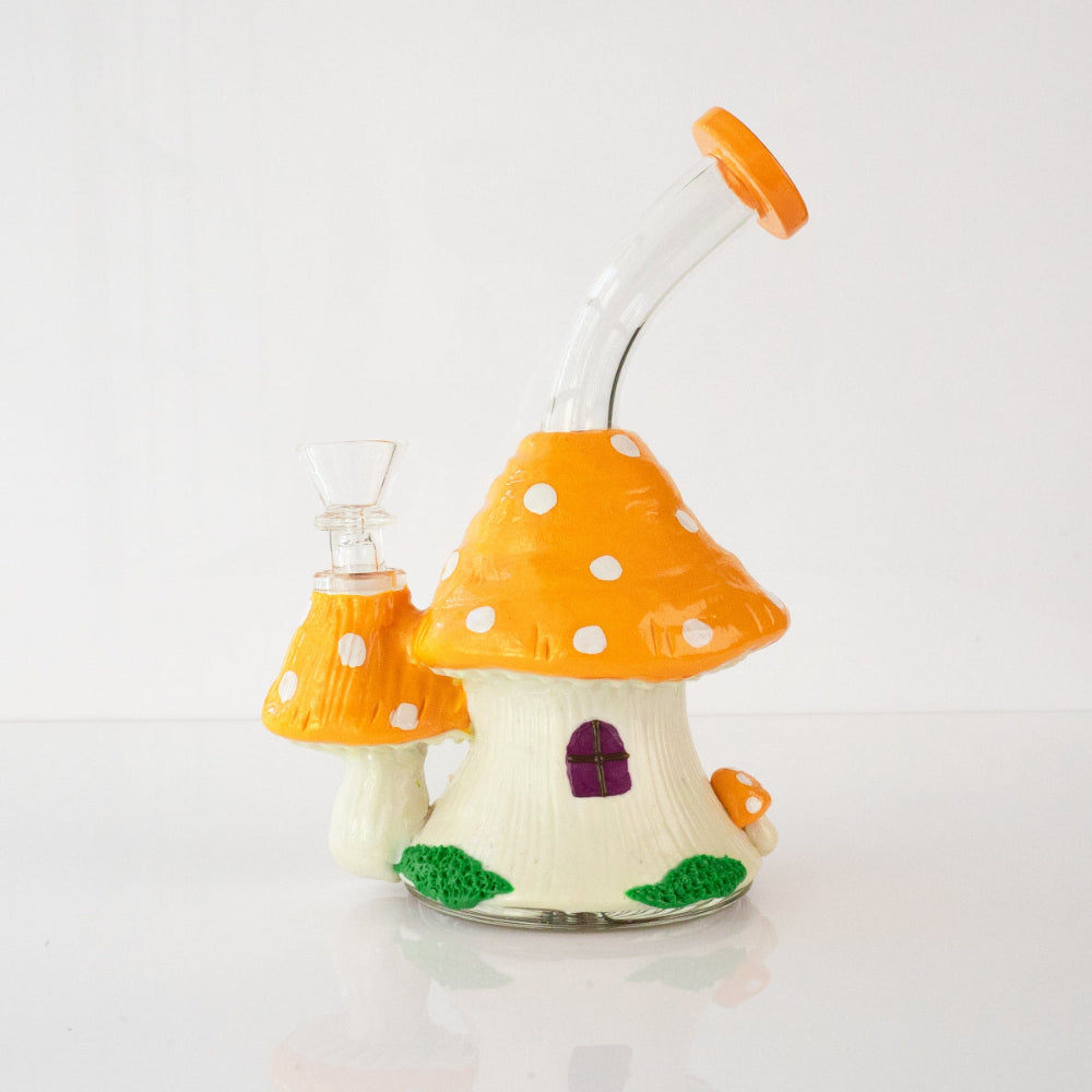 Glass mushroom house shaped bong in orange with white polka dots and curved mouthpiece on a white background