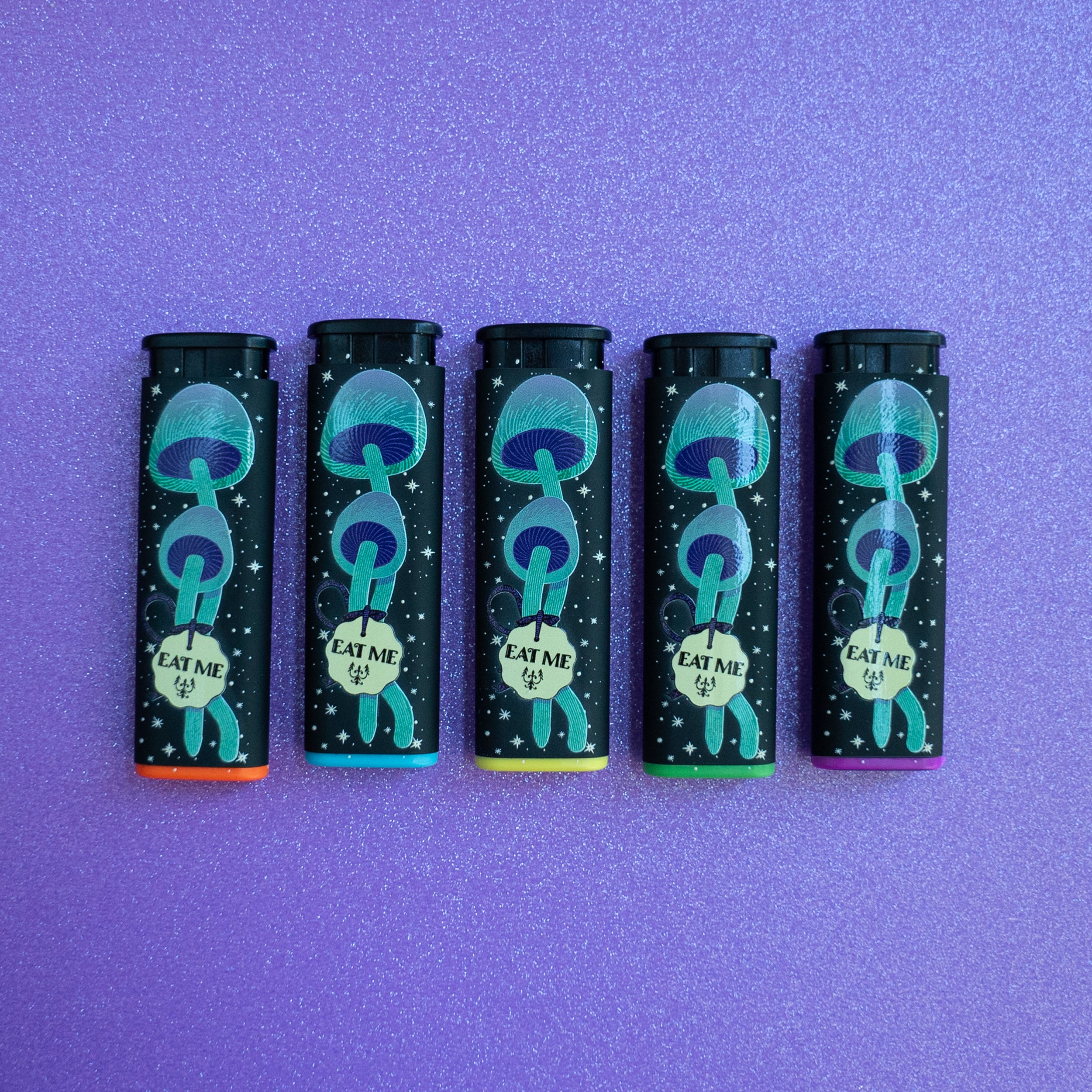 5 Feed Your Head Torch Lighters by Ella Dandelion, showcasing its windproof and refillable design. Featuring the front design, 'Drink Me' green and purple potion. And the back design, green and purple 'eat me' starry illustration. On a light purple glittery background.
