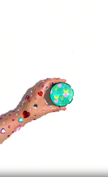 Green metal grinder with artistic designs, including plant and heart motifs, and a half-moon pattern video